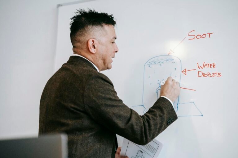 A male professional explains a diagram on a whiteboard during an educational session indoors.