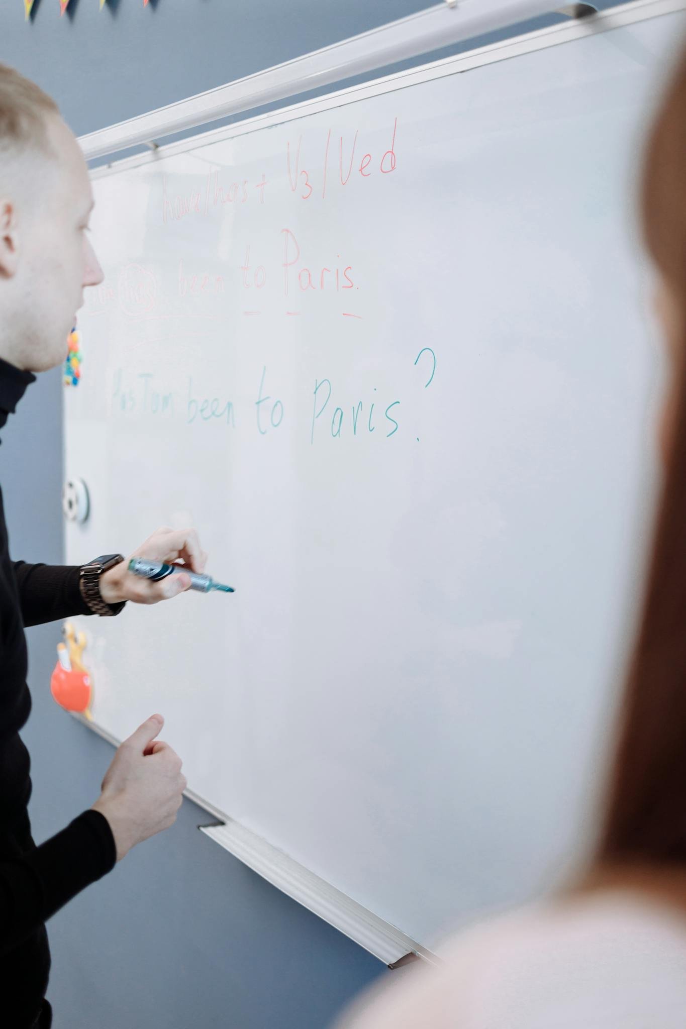 Teacher explaining English lesson using a whiteboard in a classroom setting.